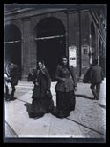Due donne attraversano la via Ugo Bassi verso la piazza del Nettuno: prospetto del portico della Gabella: Bologna