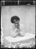 Ritratto di una donna con i gomiti appoggiati sopra un tavolino e le mani intrecciate: set fotografico allestito nel cortile interno della Biblioteca Universitaria di Bologna