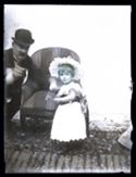Ritratto di una bambina vicino ad una poltrona e un uomo che le indica l’obiettivo fotografico: set fotografico allestito nel cortile interno della Biblioteca Universitaria di Bologna