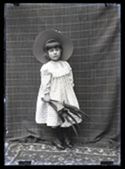 Ritratto di una bambina con un cappello in paglia e un mazzetto di fiori in stoffa: set fotografico allestito con un telo con motivo a griglia rettangolare e un tappeto