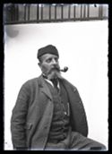 Ritratto di Olindo Guerrini con un berretto a busta in panno e la pipa in bocca: set fotografico allestito nel cortile interno della Biblioteca Universitaria di Bologna