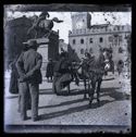 Un uomo di spalle con le mani giunte dietro la schiena e una donna che aiuta una bambina a scendere dal calesse fermo vicino alla statua equestre di Vittorio Emanuele II: prospetto del Palazzo Comunale in piazza Vittorio Emanuele II: Bologna