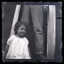 Una bambina davanti all’ingresso di una casa e le gambe di un uomo sull’uscio