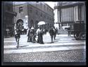 Un uomo e due donne attraversano la via Carlo Alberto: prospetto della via Mercanti con il palazzo della Ragione e del palazzo Giureconsulti sulla via Carlo Alberto: Milano