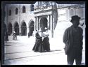 Un uomo con la pipa in bocca e due donne a passeggio verso la piazza del Nettuno: prospetto del portico e del portale d’ingresso del Palazzo Comunale in piazza Vittorio Emanuele II: Bologna