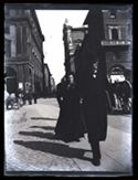 Un uomo e una donna a passeggio in piazza del Nettuno: incrocio delle vie Ugo Bassi, dell'Indipendenza e Rizzoli con veduta sulla via dell'Indipendenza: Bologna