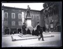 Un giovane uomo a passeggio che guarda l’obiettivo fotografico e quattro uomini seduti sul monumento con la statua di Vittorio Emanuele II e quella allegorica dell’Italia: piazza della Cattedrale: Ferrara