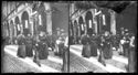 Un uomo che guarda l’obiettivo fotografico e tre donne a passeggio e le persone davanti al portico della casa Coccapani per il passaggio della processione della Beata Vergine di San Luca in via dell’Indipendenza: Bologna maggio 1892
