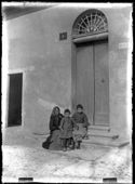 Un’ anziana donna e due bambine sedute sugli scalini d’ingresso del numero civico 509