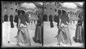 Una donna di spalle con il parasole che fa conversazione con un uomo e una giovane donna che guarda l’obiettivo fotografico: prospetto del Palazzo Comunale fra le piazze Vittorio Emanuele II e del Nettuno: Bologna