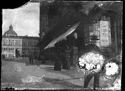 Un uomo che guarda l’obiettivo fotografico all’angolo con la via d’Azelio e due donne a passeggio in piazza Vittorio Emanuele: prospetto del Portico e Palazzo dei Banchi: Bologna