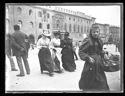 Una giovane donna con un paniere che guarda l’obiettivo fotografico e tre donne a braccetto a passeggio in piazza Vittorio Emanuele II: prospetto del Palazzo Comunale fra le piazze Vittorio Emanuele II e del Nettuno: Bologna