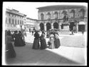 Un gruppetto di donne di spalle in piazza Vittorio Emanuele II davanti alla statua equestre di Vittorio Emanuele II e al palazzo del Podestà con l’esposizione artistica Francesco Francia: prospetto del Palazzo Comunale in piazza del Nettuno: Bologna