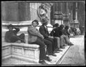 Un bambino che guarda l’obiettivo fotografico e alcuni uomini seduti sullo zoccolo fra il portale mediano, detto porta Magna, e il portale destro della basilica di San Petronio: piazza Vittorio Emanuele II: Bologna