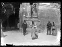 Una donna con una brocca e un secchio, un uomo con la bombetta e il bastone da passeggio e un uomo e una donna a passeggio, davanti alle colonne del portale d’ingresso del Palazzo Comunale: piazza Vittorio Emanuele 6: Bologna