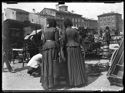 Due donne di spalle guardano la merce di un rigattiere al mercato in piazza dell’Otto Agosto: prospetto del lato sud-ovest della piazza: Bologna