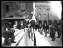 Un uomo seduto che guarda l’obiettivo fotografico e una donna con un infante in braccio sulla scalinata della basilica di San Petronio: piazza Vittorio Emanuele II: prospetto del palazzo dei Notai sulla via de’ Pignattari e dell’ala sinistra del Palazzo Comunale: Bologna