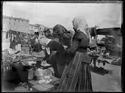 Sei donne davanti alla merce esposta su un banco al mercato in piazza dell’Otto Agosto: prospetto del lato ovest della piazza: Bologna