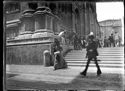 Un uomo e una donna a passeggio davanti alla scalinata e le persone sullo zoccolo e sul sagrato della basilica di San Petronio: piazza Vittorio Emanuele II: prospetto del palazzo dei Notai sulla via de’ Pignattari: Bologna