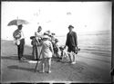 Un bambino di spalle con la rete per la pesca, un uomo con il parasole, una giovane donna e un giovane uomo che guardano l’obiettivo fotografico e un gruppetto di bambini sulla spiaggia: Bellaria