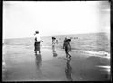 Una donna di spalle a passeggio, due bambini con un cappello di paglia sulla battigia e i bagnanti in mare: Bellaria