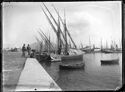 Quattro uomini sul molo del porto di Napoli e le barche con i pescatori: sullo sfondo il Vesuvio