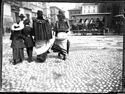 Due bambini e due donne di spalle a passeggio verso la piazza del Nettuno e un tramway a cavallo in sosta vicino al Voltone del Podestà: prospetto delle vie dell’Indipendenza e Rizzoli: Bologna