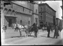 Un calesse con due uomini e un vetturino e una guardia che fanno conversazione davanti all’ufficio delle regie poste e il tramway a cavallo numero 27: piazza del Nettuno: prospetto della via dell’Indipendenza: Bologna