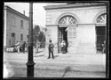 L’ interno di una stazione ferroviaria con due passeggeri in attesa sul marciapiede del binario e una donna e un ferroviere sulla porta d'ingresso del fabbricato viaggiatori