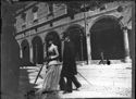 Un uomo con la bombetta e una donna con un cappellino attraversano la via dell’Indipendenza: prospetto del portico della casa Coccapani: Bologna
