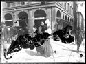Una donna con un infante in braccio attraversa la via Ugo Bassi verso la piazza del Nettuno: prospetto del portico della Gabella: incrocio delle vie Ugo Bassi e dell’Indipendenza: Bologna