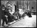 Un gruppo di uomini con il cappello e il bastone da passeggio seduti sullo zoccolo fra il portale mediano, detto porta Magna, e il portale destro della basilica di San Petronio: piazza Vittorio Emanuele II: Bologna