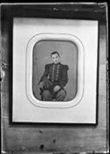 Ritratto di Olindo Guerrini con la divisa da sergente della guardia nazionale da una fotografia ritoccata, incorniciata e appesa allo schienale in legno di una sedia capovolta