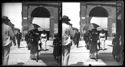 Un uomo di spalle, una donna con il parasole, una bambina con un cappellino e altre persone attraversano la via dell’Indipendenza: prospetto del portico della Gabella: Bologna